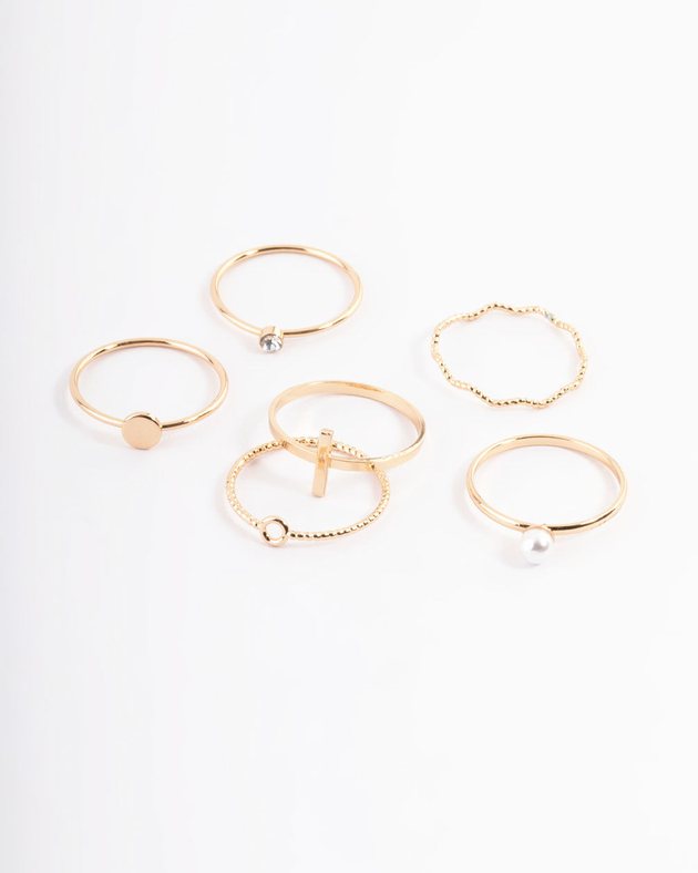 six dainty gold rings, some with a small faux pearl or crystal