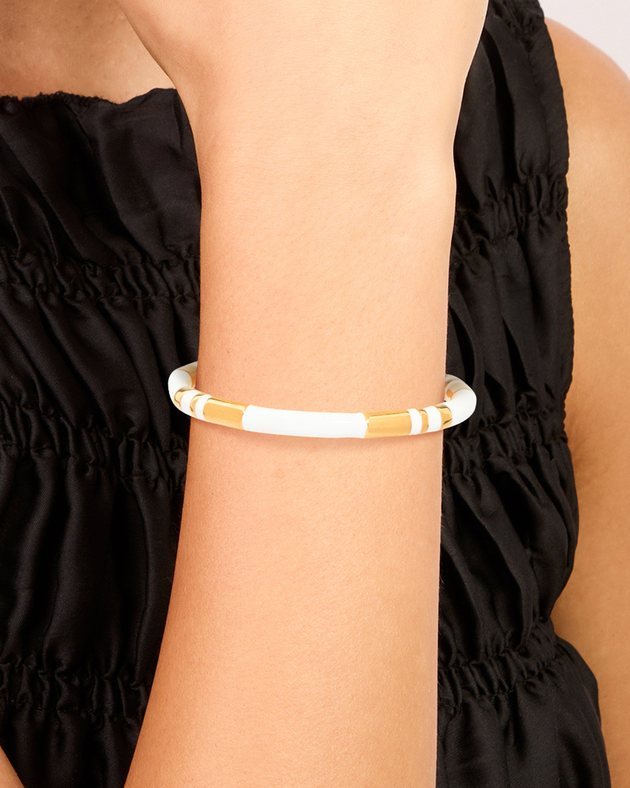 model's wrist wearing a white enamel cuff with gold stripes