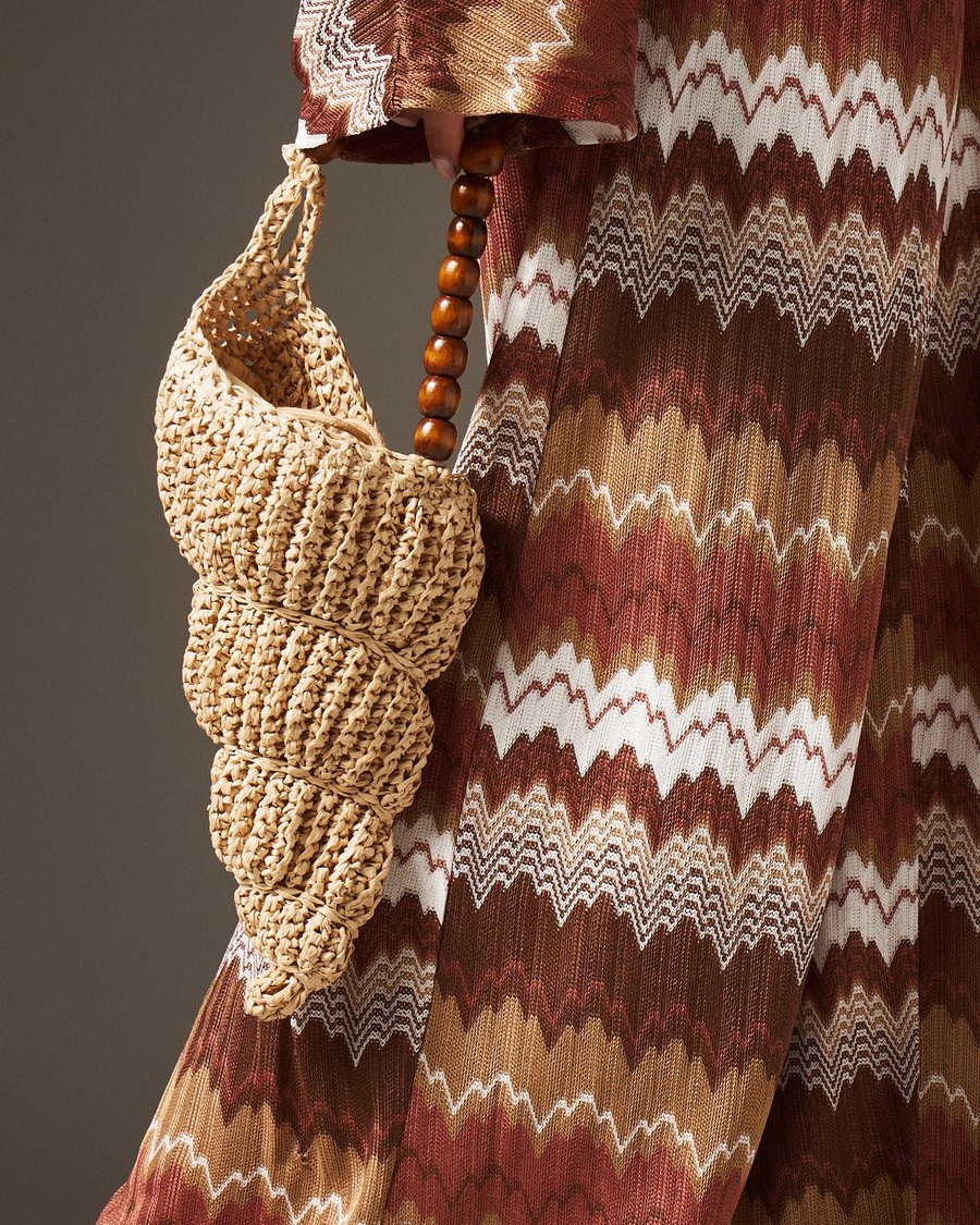 close-up of a natural crochet raffia shell-shaped mini bag with a wooden bead handle, held against a zigzag knit dress