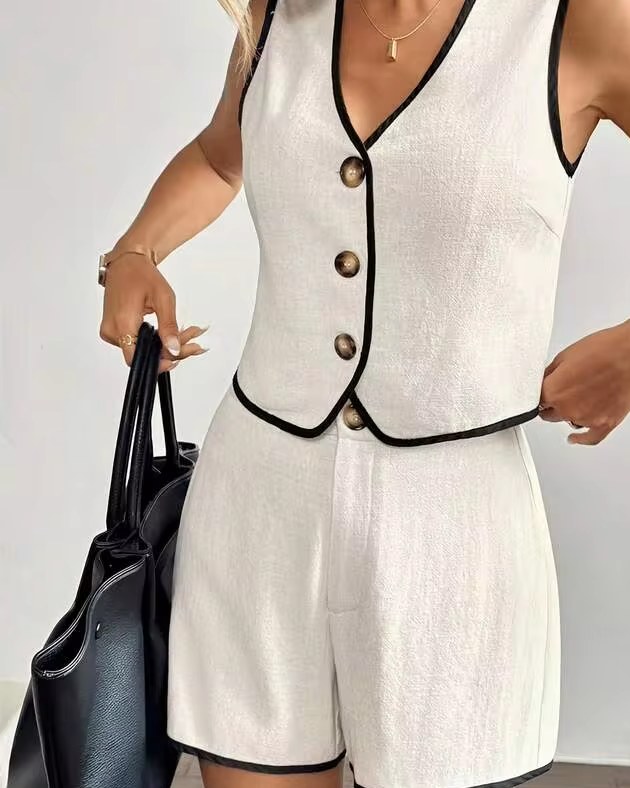 woman in a white linen button vest and matching shorts with black trim, holding a black tote