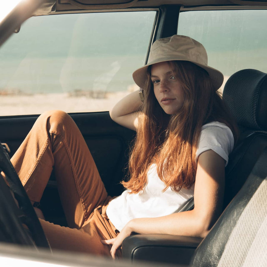 woman in an off-white cotton bucket hat sitting in a vintage car by the beach