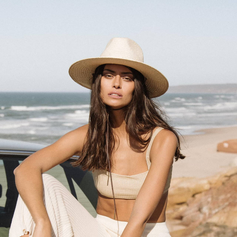 woman in a white palm straw hat sitting by the beach